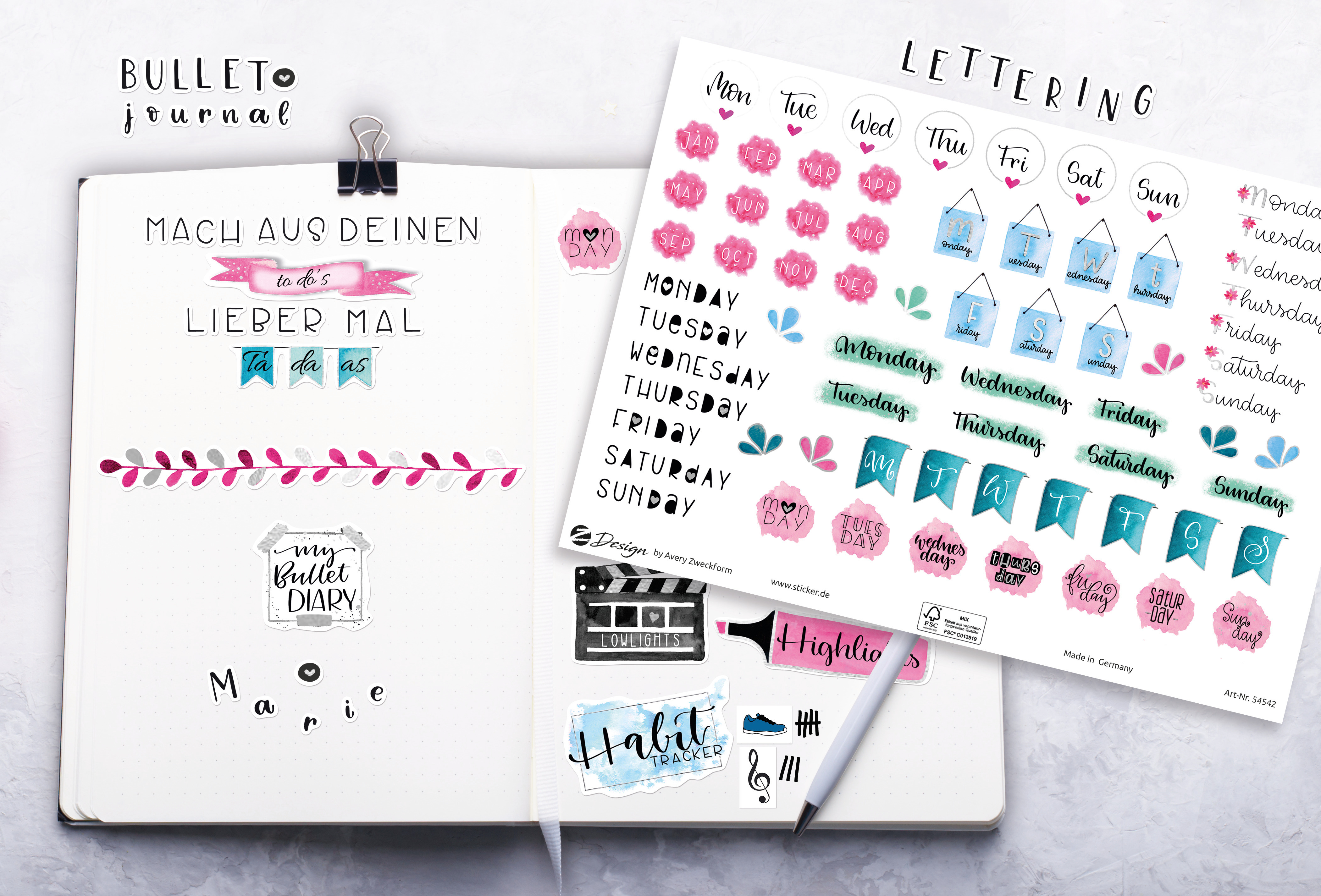 Ein Notizbuch mit Aufklebern und einem Stift. Aufkleber umfassen Schriftzüge und Bullet-Journal-Elemente in Rosa und Blau.