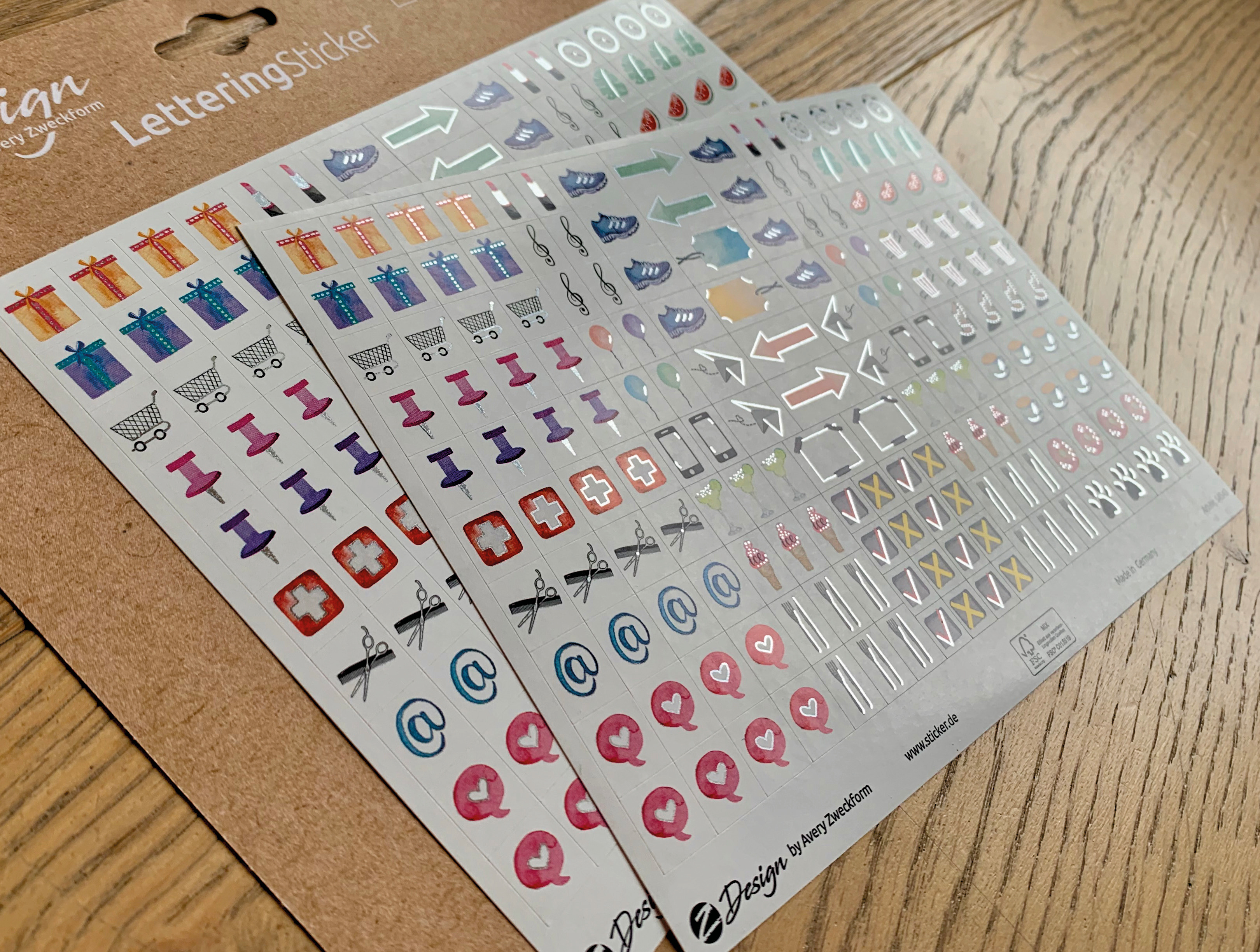 Aufkleberbögen mit verschiedenen Symbolen, darunter Geschenke, Einkaufswagen, Reißzwecken und Social-Media-Symbole.