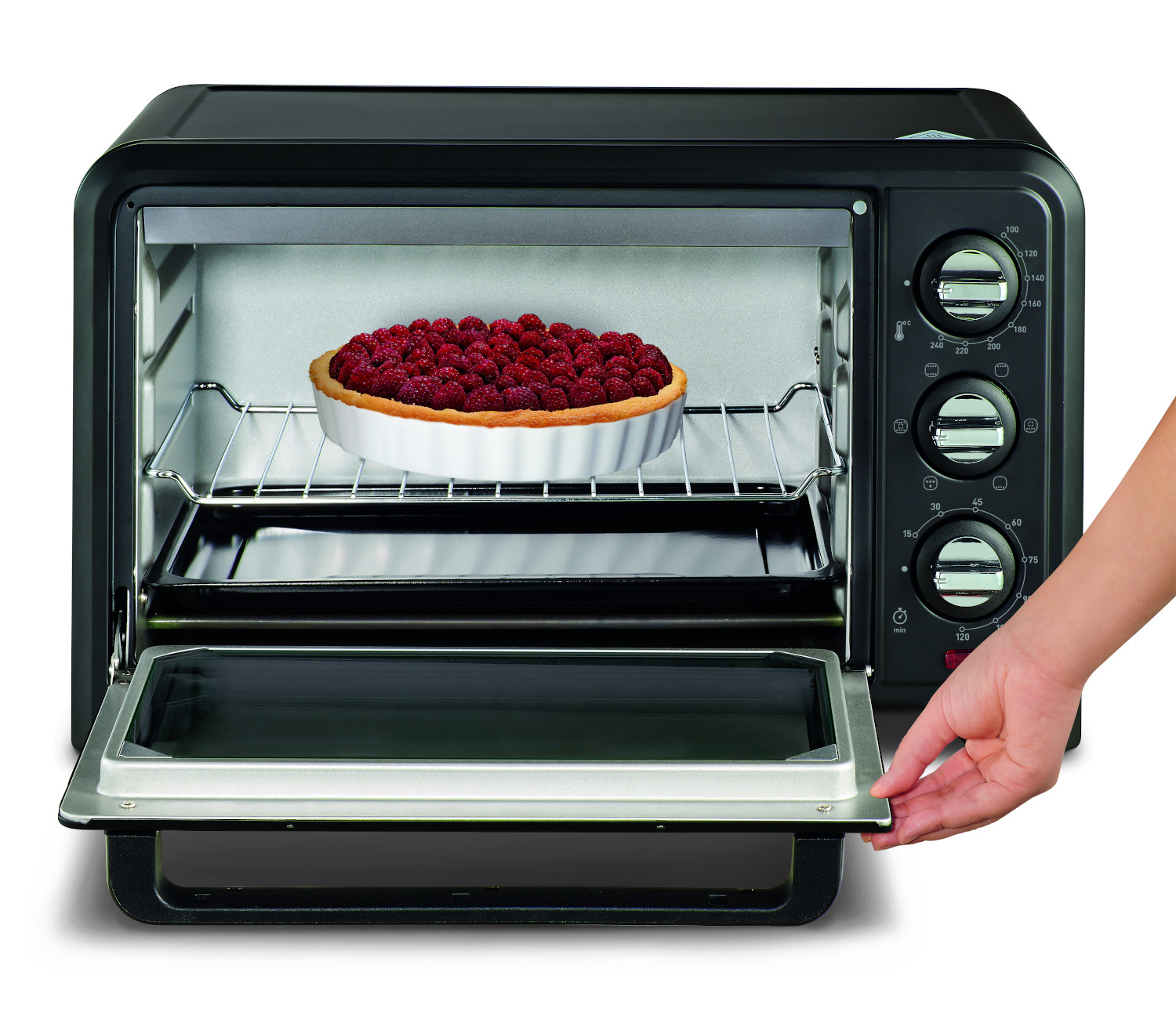 A black toaster oven with the door open and a pie inside, a hand is on the right.