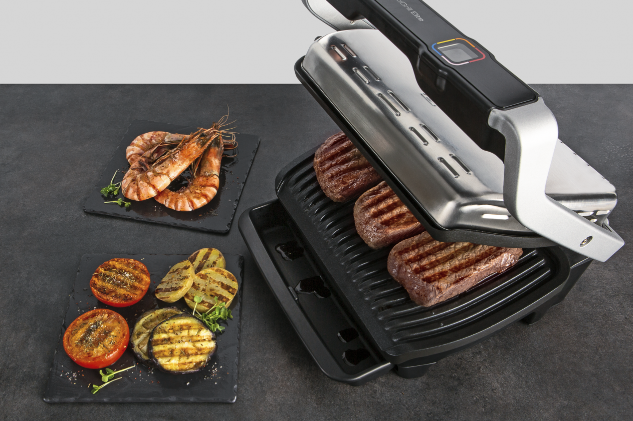 Grilled food on a grill, including shrimp, steaks, and vegetables on plates.