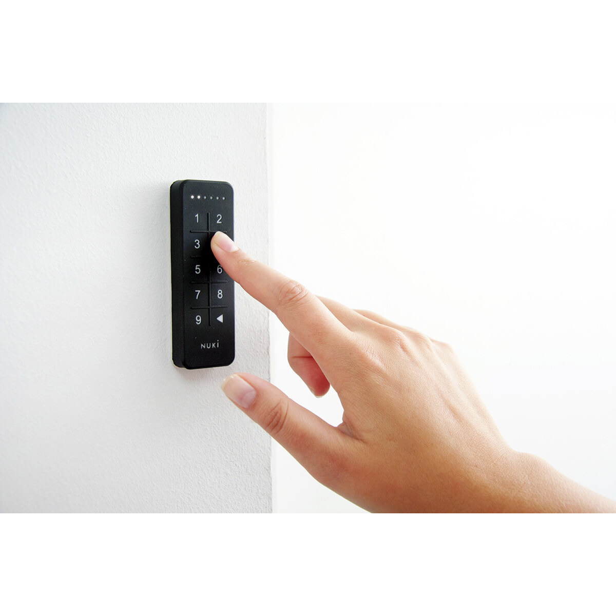 Una mano presionando un botón en un teclado negro de cerradura de puerta inteligente.