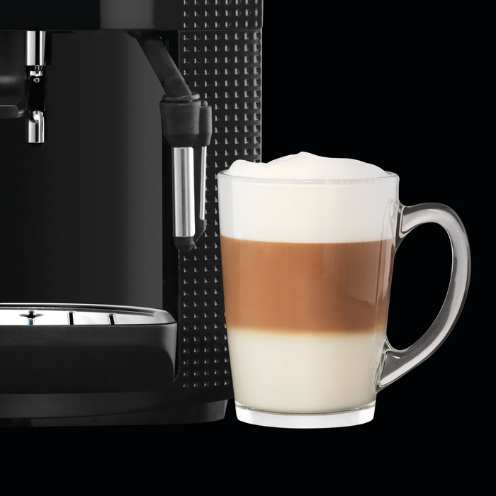Latte egy átlátszó pohárban egy fekete kávéfőző mellett. Fekete háttér.