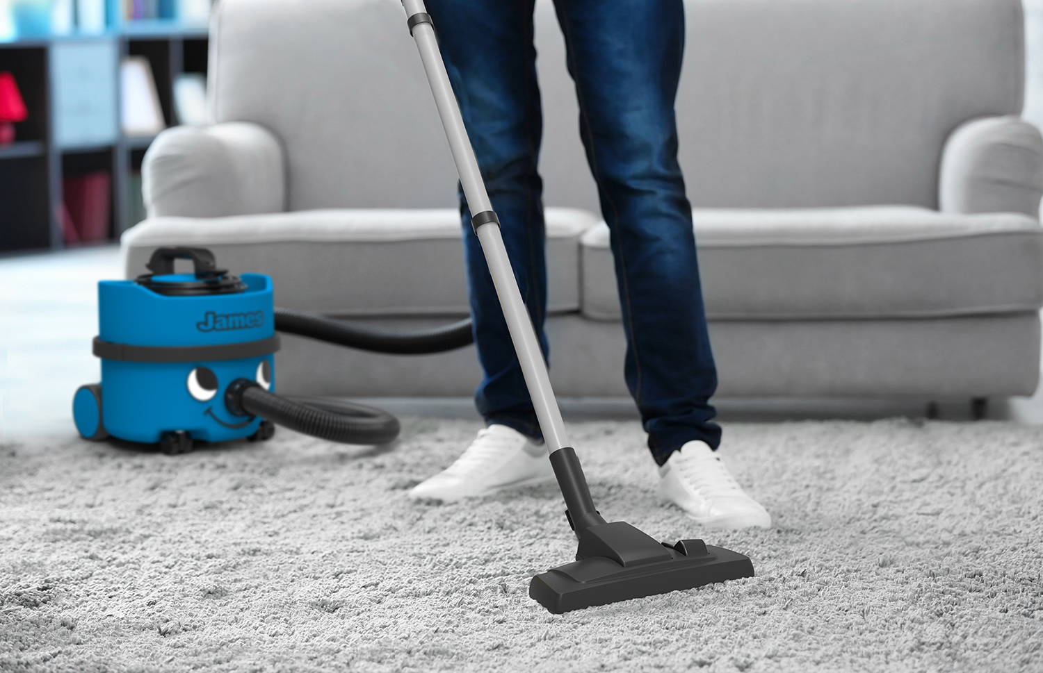 A man vacuums a grey carpet with a blue and grey vacuum cleaner.
