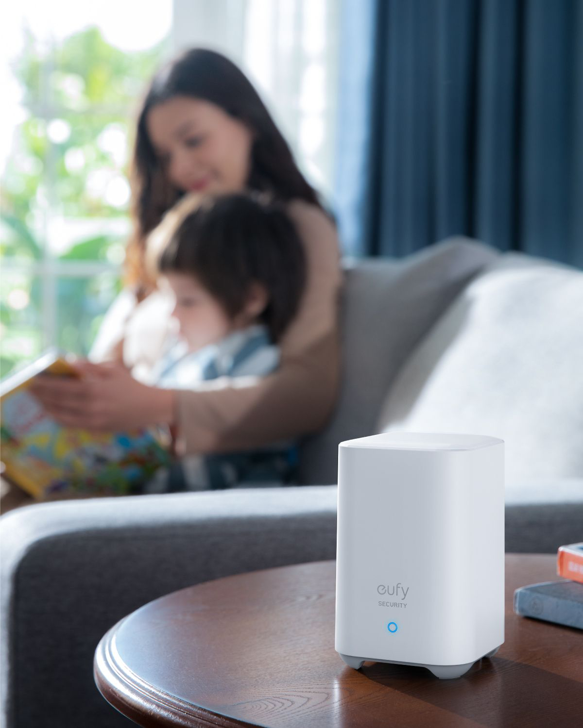 Witte eufy security homebase, op tafel, met mensen op de achtergrond.