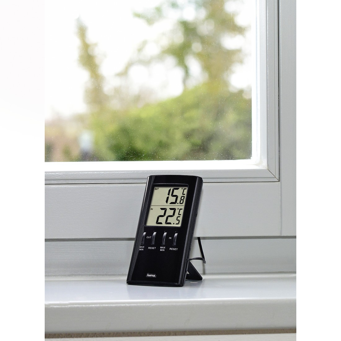 Zwarte digitale thermometer die buiten- en binnentemperaturen weergeeft, op een vensterbank.