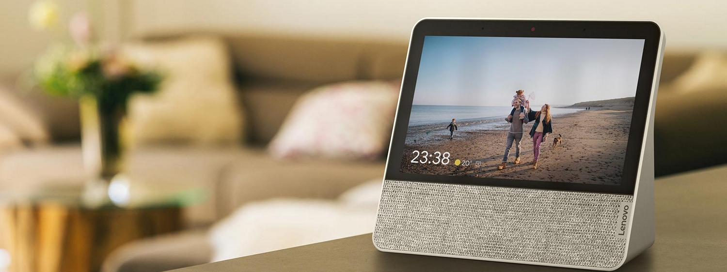 Pantalla inteligente en mesa, muestra familia en playa; sofá al fondo.