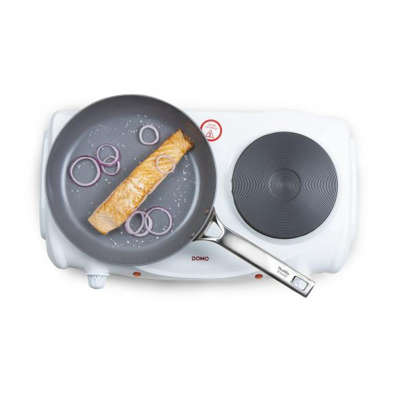 A pan with salmon and red onions on a white cooktop.