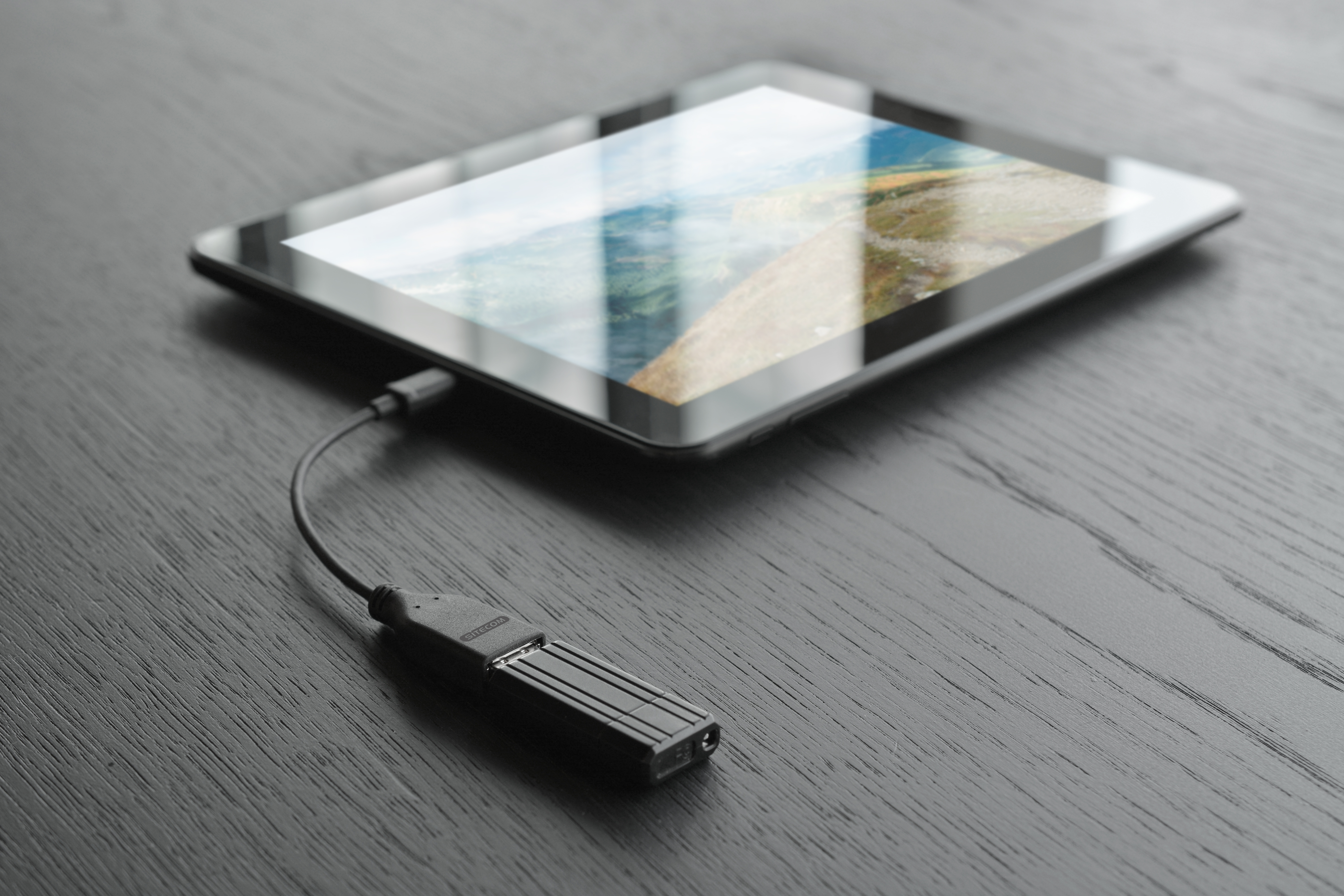 Tablet on wood surface with a charging adapter plugged into it.