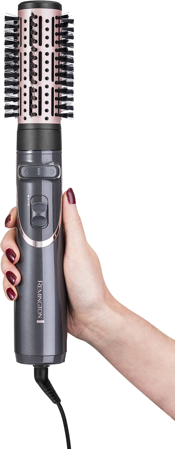 A woman's hand holds a Remington hair styler. A pink and black brush is attached.