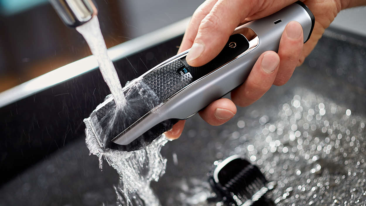 Een hand houdt een zilver-zwarte elektrische scheerapparaat onder stromend water. Water stroomt over de kop.