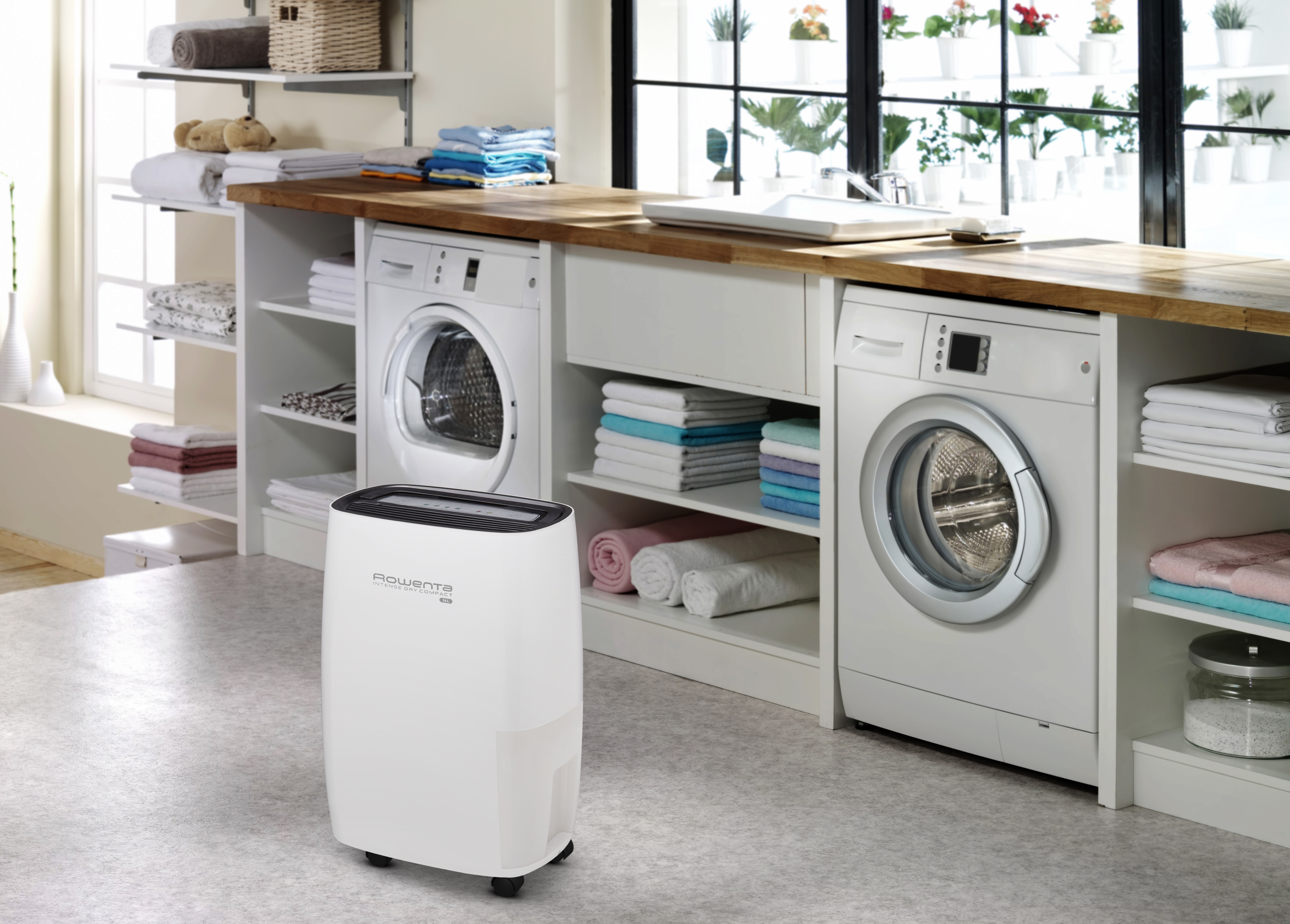 Un déshumidificateur blanc entre une machine à laver et un sèche-linge dans une buanderie.