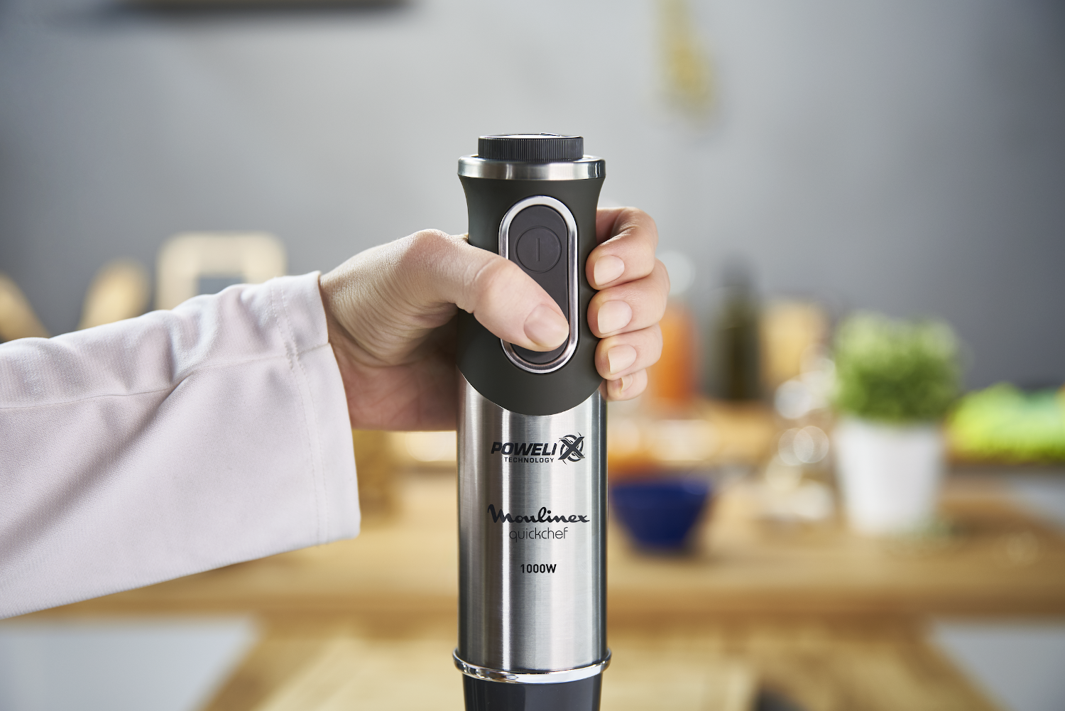 Person holding a black and silver Moulinex QuickChef hand blender.