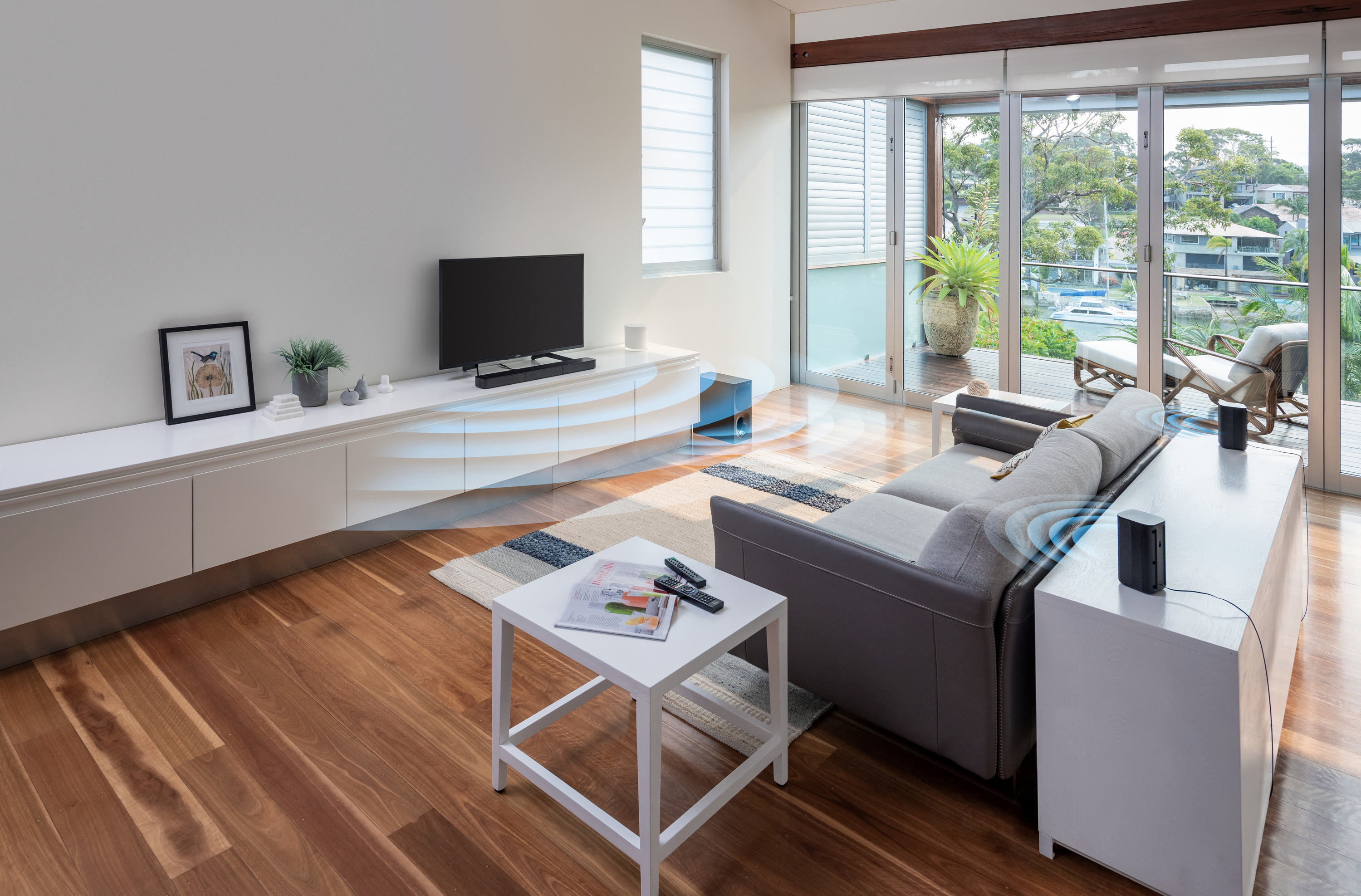 Wohnzimmer mit Sofa, Lautsprechern und Couchtisch, mit blauen Schallwellen.