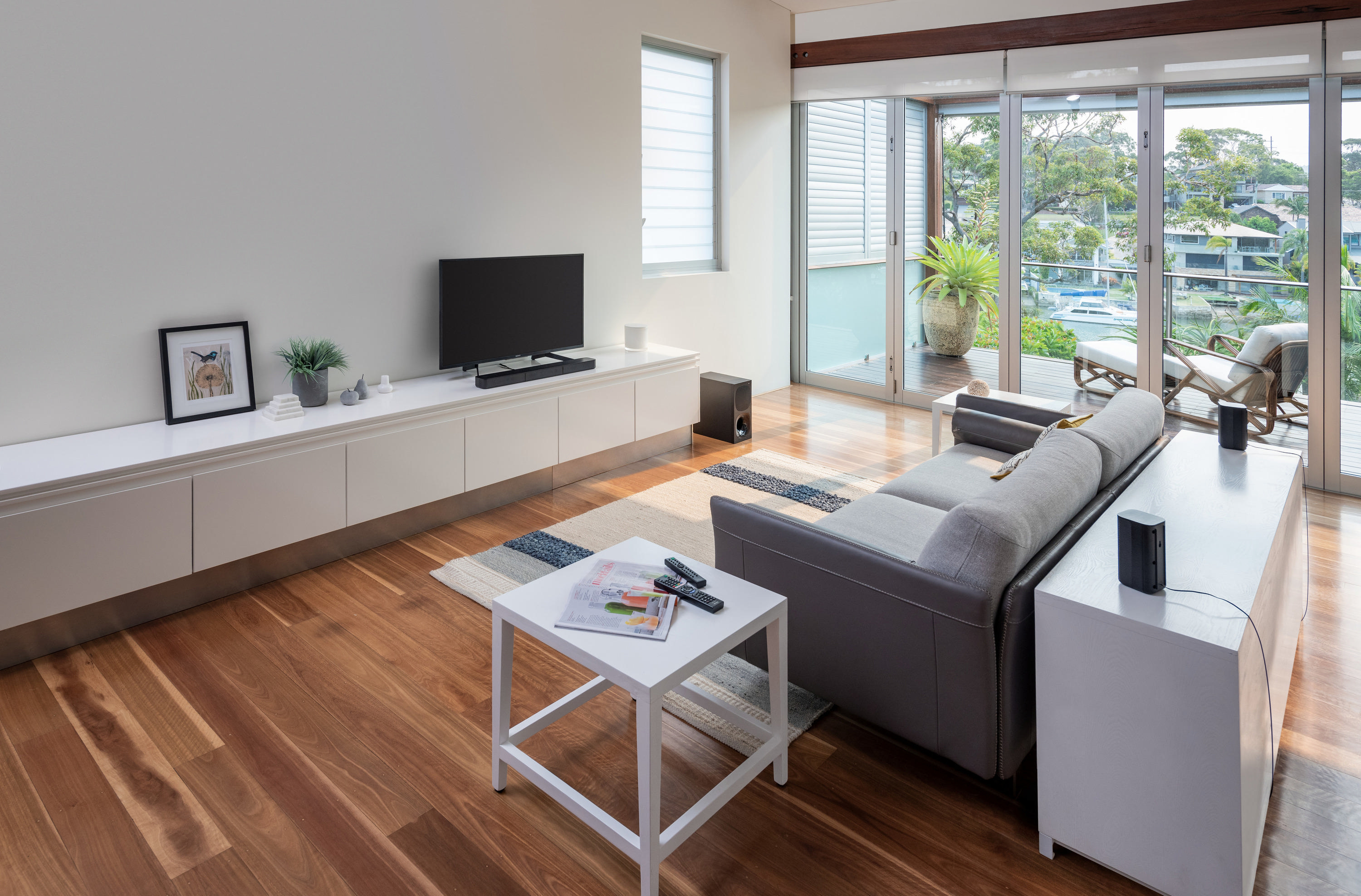 Wohnzimmer mit weißen Wänden, Holzboden und Blick auf einen Balkon mit Wasser.