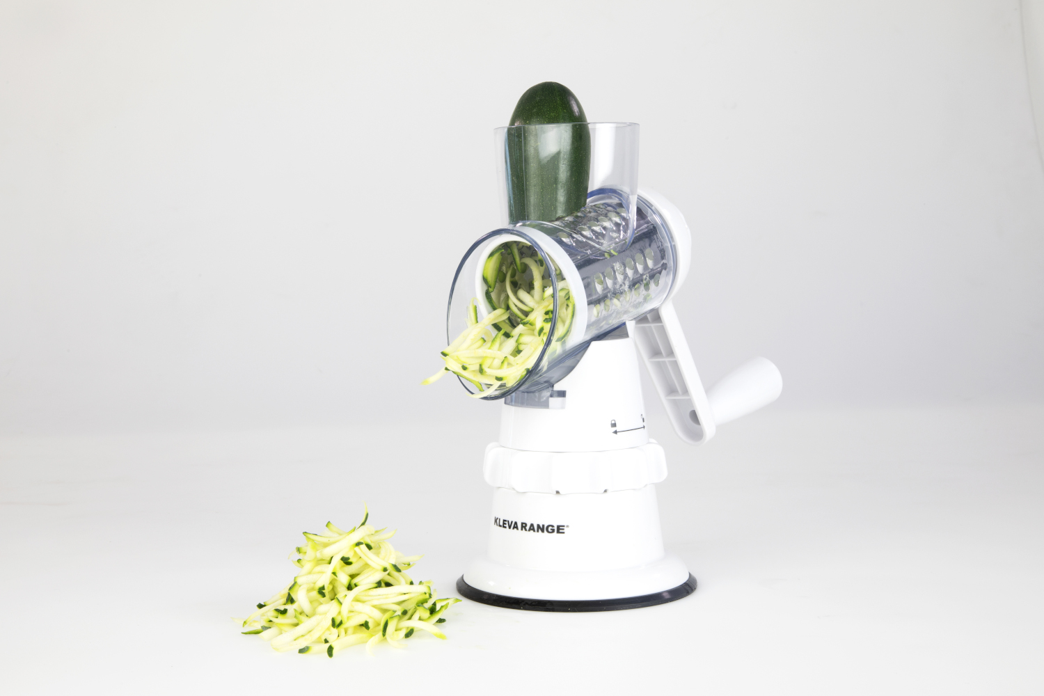 Un spiraliseur de légumes blanc avec des courgettes à l'intérieur et un tas de courgettes spiralées à côté.