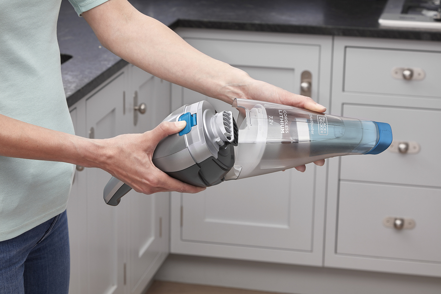 A person's hands holding a cordless handheld vacuum cleaner. The vacuum is gray and blue.