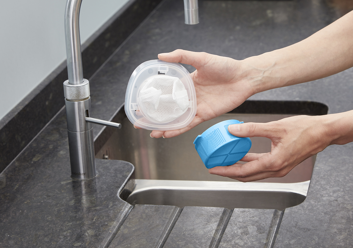 Hands holding disassembled vacuum cleaner parts over a stainless steel sink.