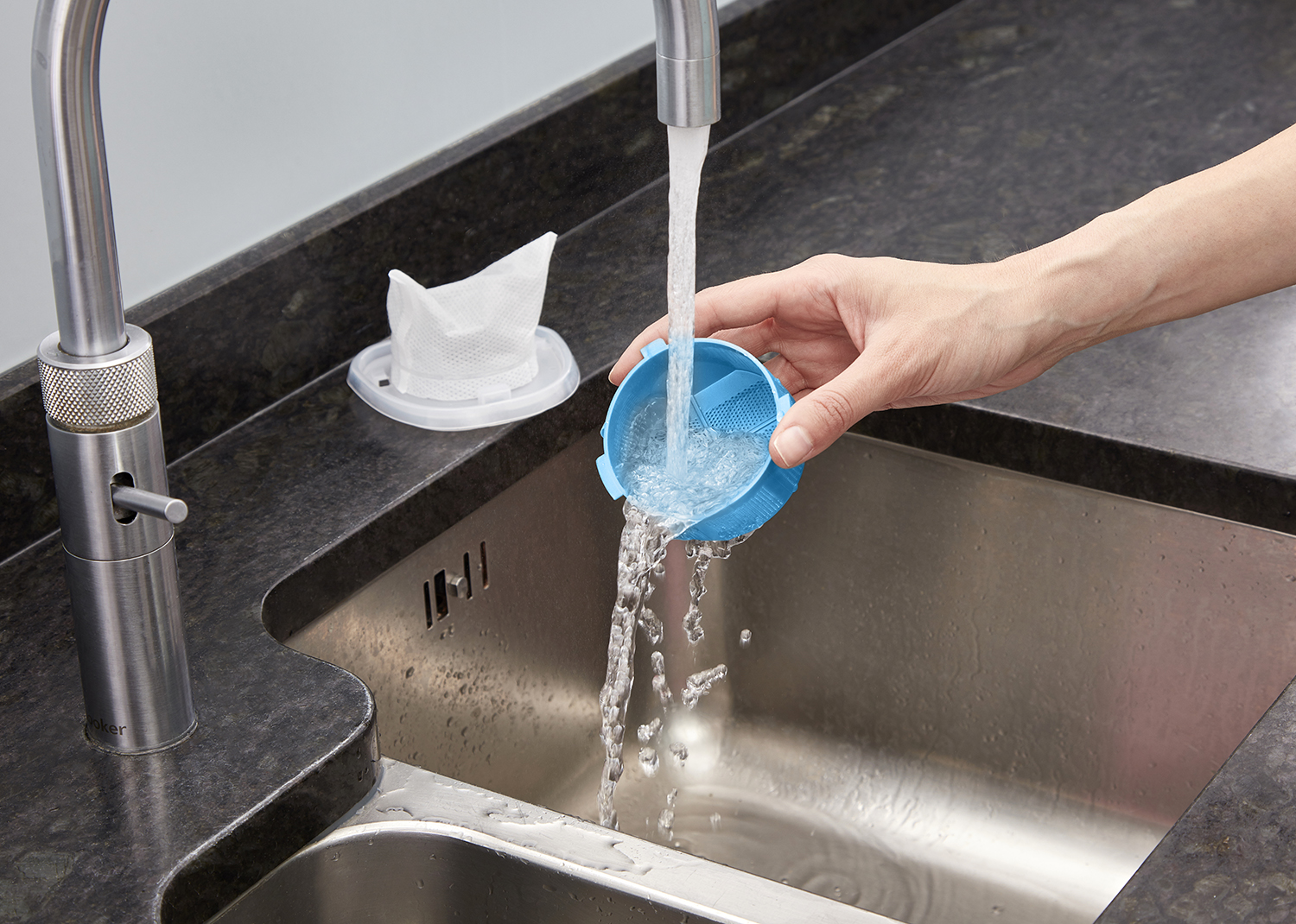 A hand washing a blue dishwasher filter under a silver faucet.