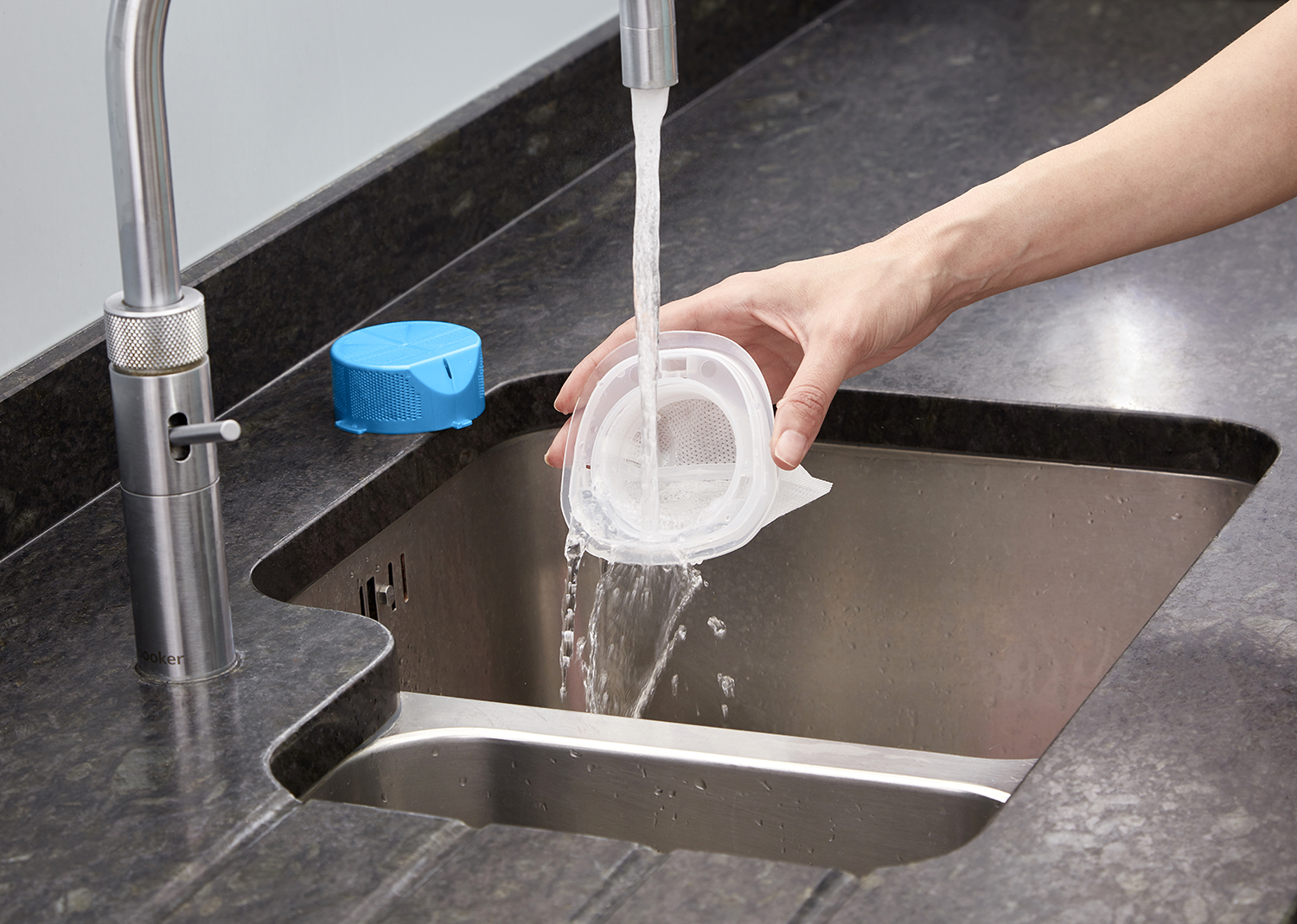 A sink with a faucet. A filter is being rinsed under the running water.