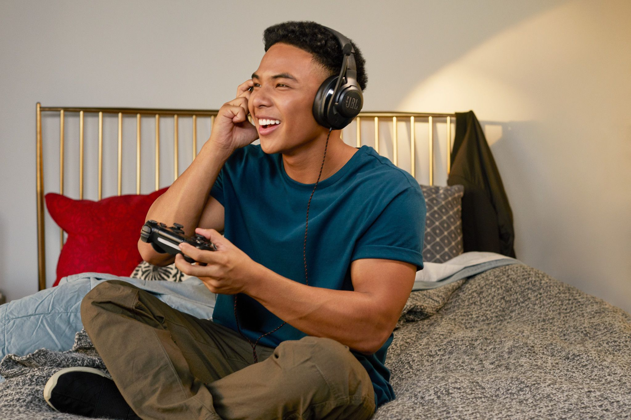 Een jonge man zit met gekruiste benen op een bed, met een koptelefoon en een gamecontroller.