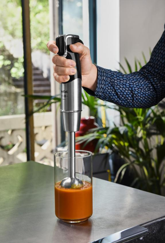 Personne mixant de la soupe avec un mixeur plongeant Tefal dans un verre. Soupe orange visible.
