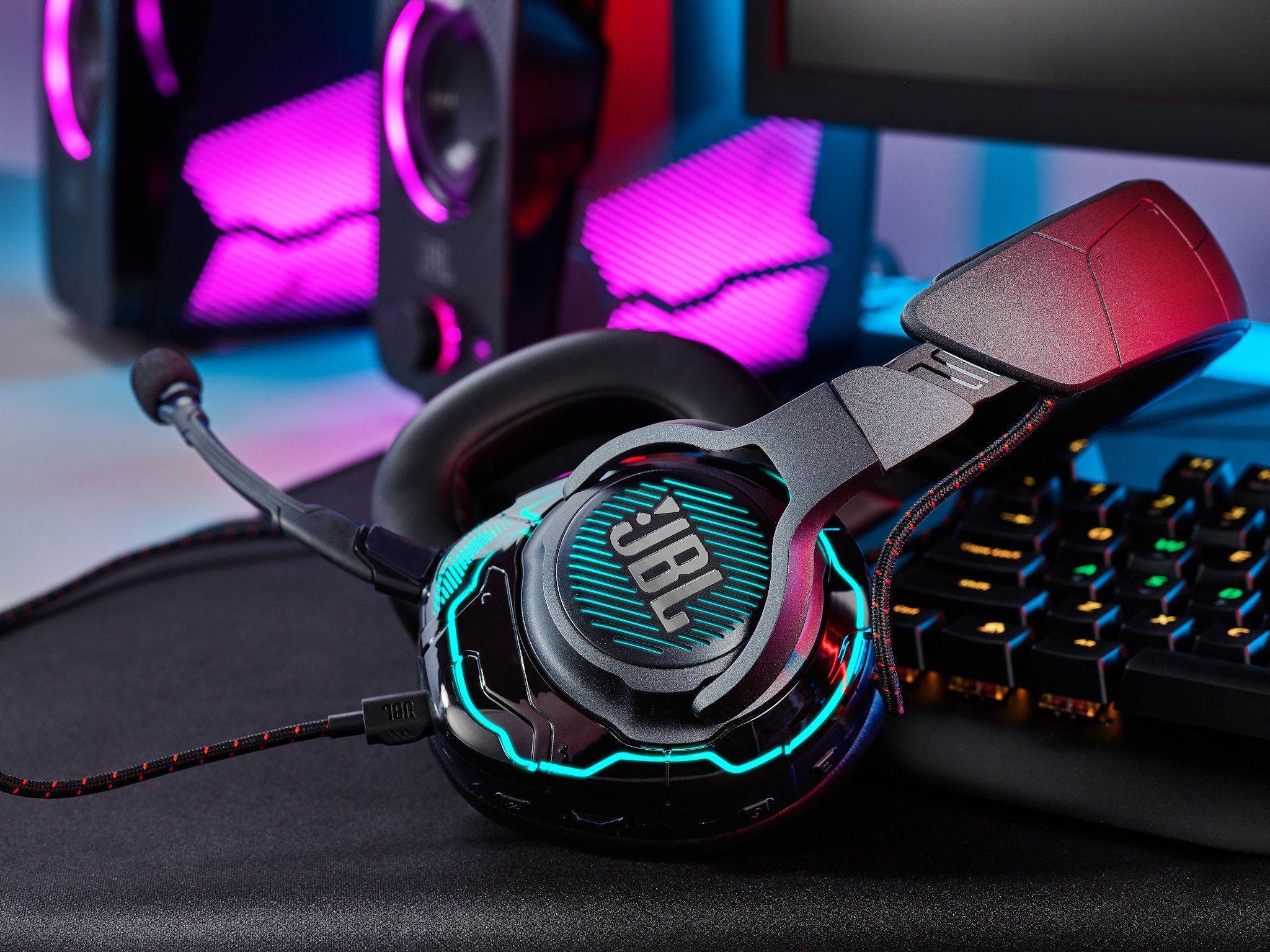 Gaming headset met JBL logo, verlicht met blauwe en rode lichten, en een zwart toetsenbord op de achtergrond.