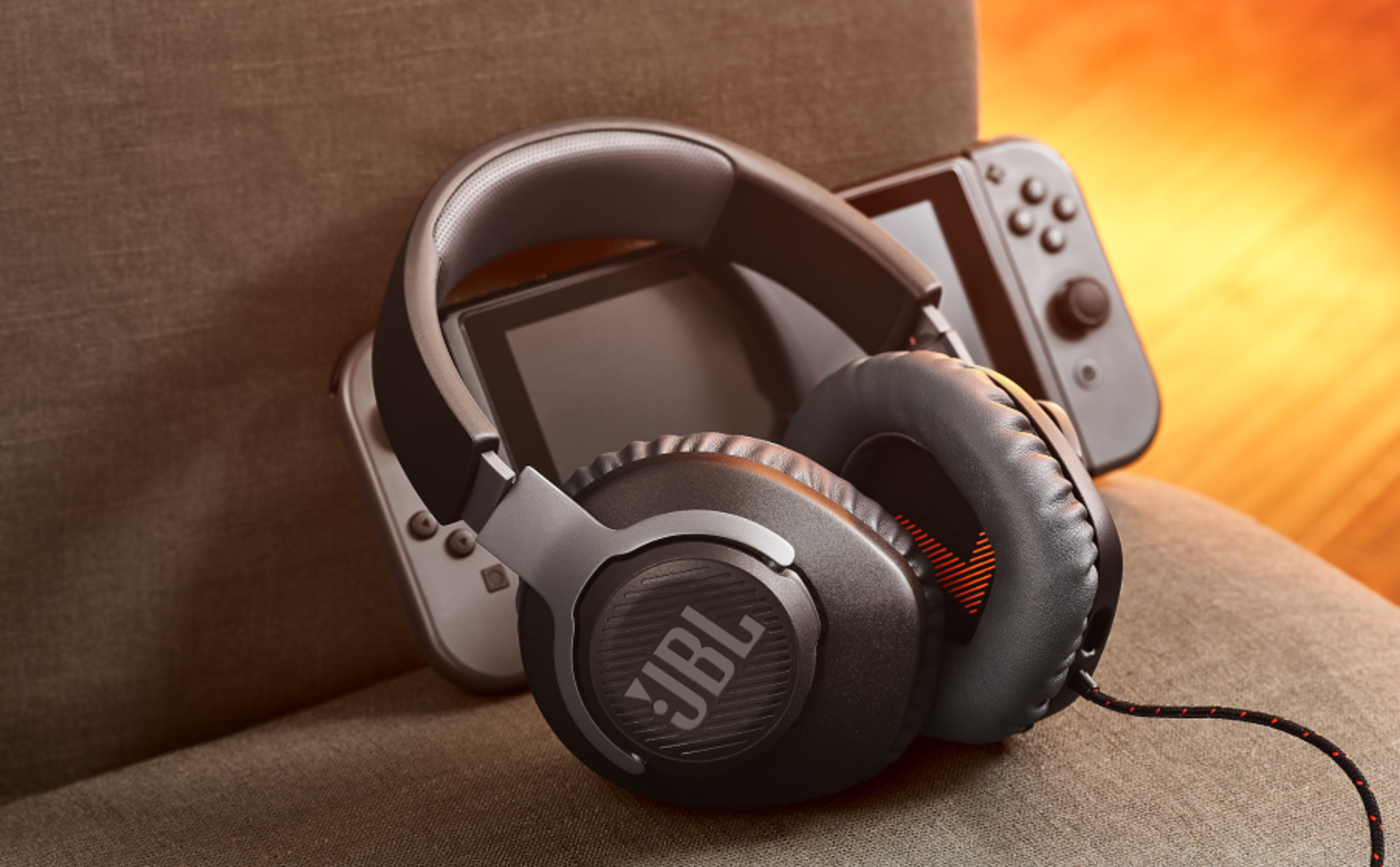JBL gaming headset en Nintendo Switch op een bank. Gezellige, warme verlichting.