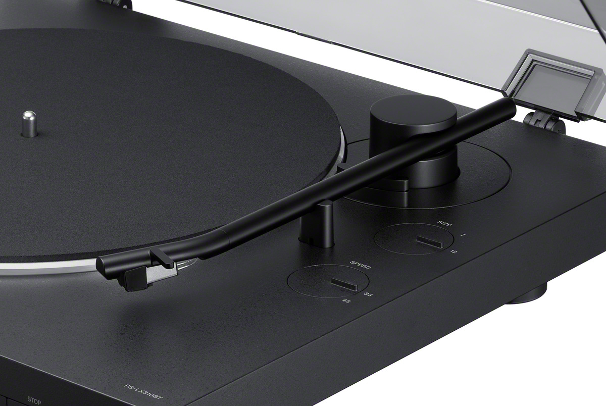 Black turntable with arm and controls. White background. Close-up view.