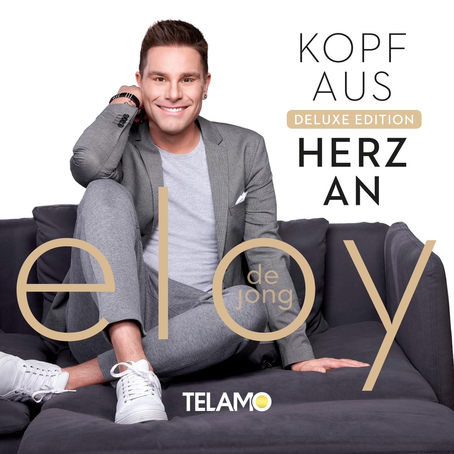 Eloy de Jong Albumcover, sitzt auf einem Sofa, trägt grauen Anzug und weiße Sneaker.