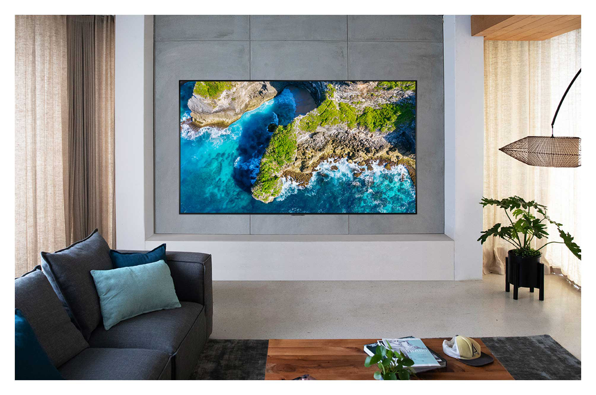 Wohnzimmer mit großem Fernseher, der eine Meereslandschaft, Sofa und Holztisch zeigt.