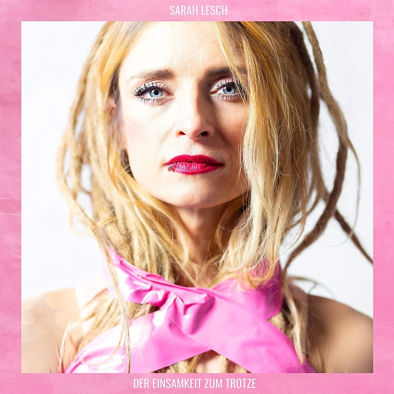 Frau mit blonden Dreadlocks, pinkem Schal, rotem Lippenstift, pinkem Hintergrund.
