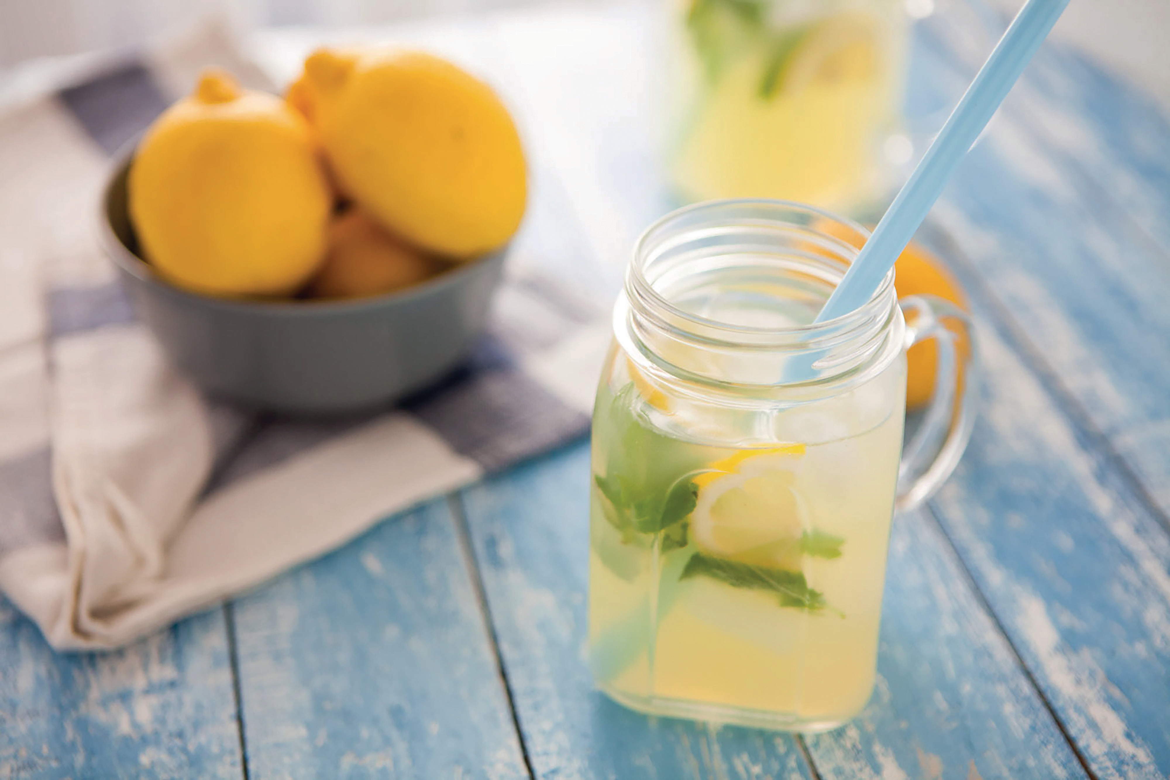 Ein Einmachglas Limonade mit Minze und einer Zitronenscheibe. Eine Schüssel mit Zitronen steht daneben.
