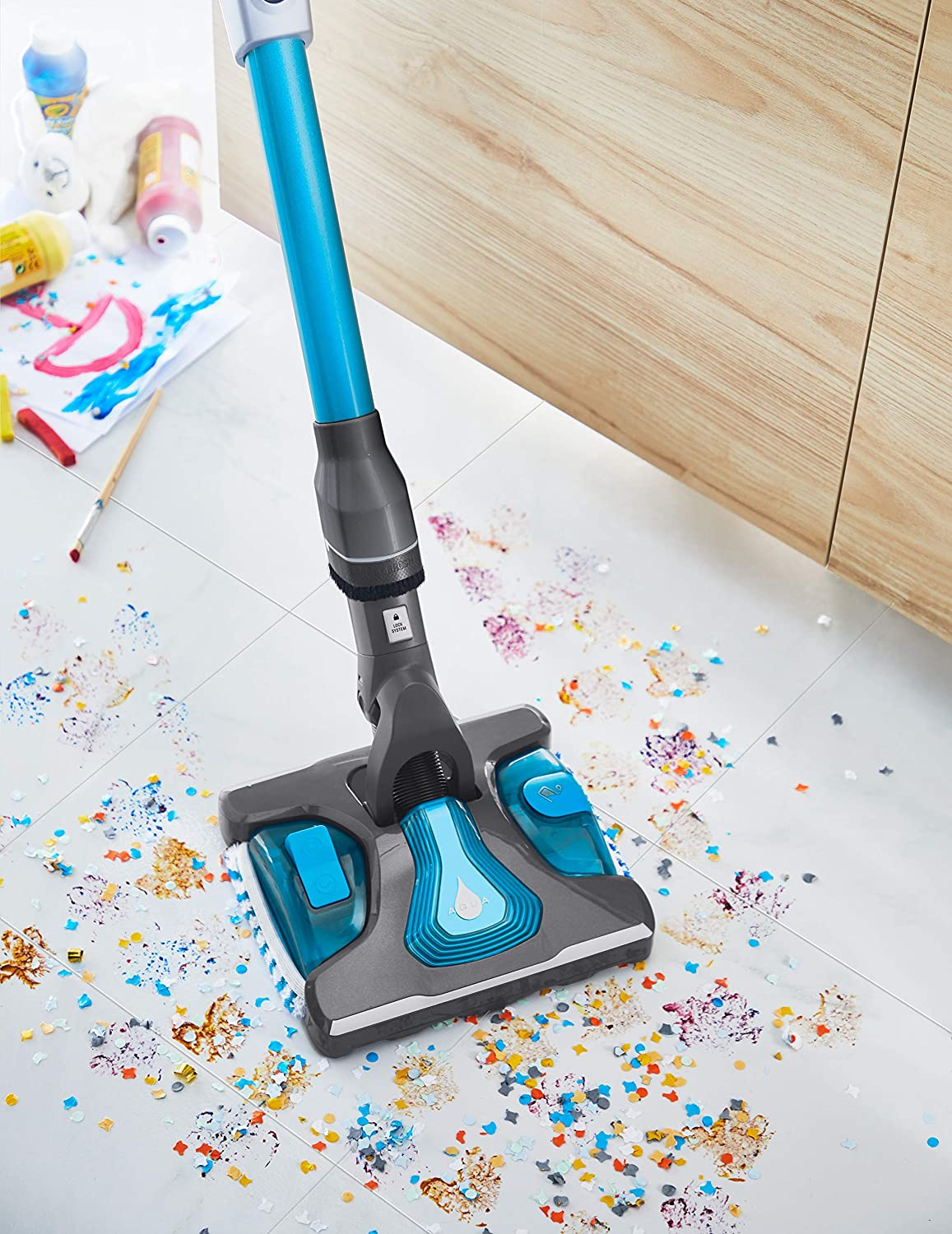 Een vloer wordt gestofzuigd met een blauw-grijze stofzuiger. Confetti op de vloer.
