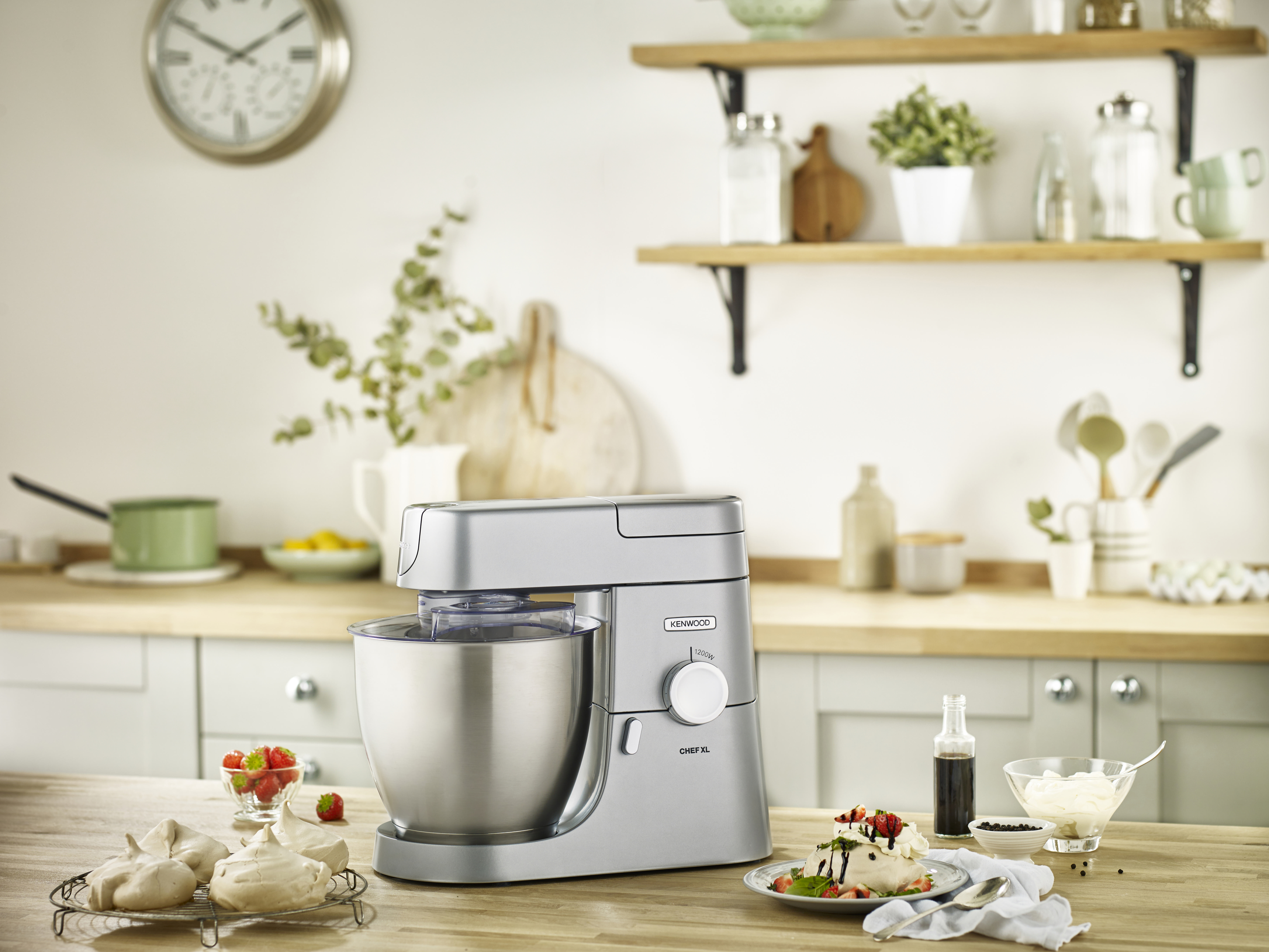 Küchenszene mit silbernem Küchenmixer, Baiser, Erdbeeren und einer Flasche. Holz-Arbeitsplatte.