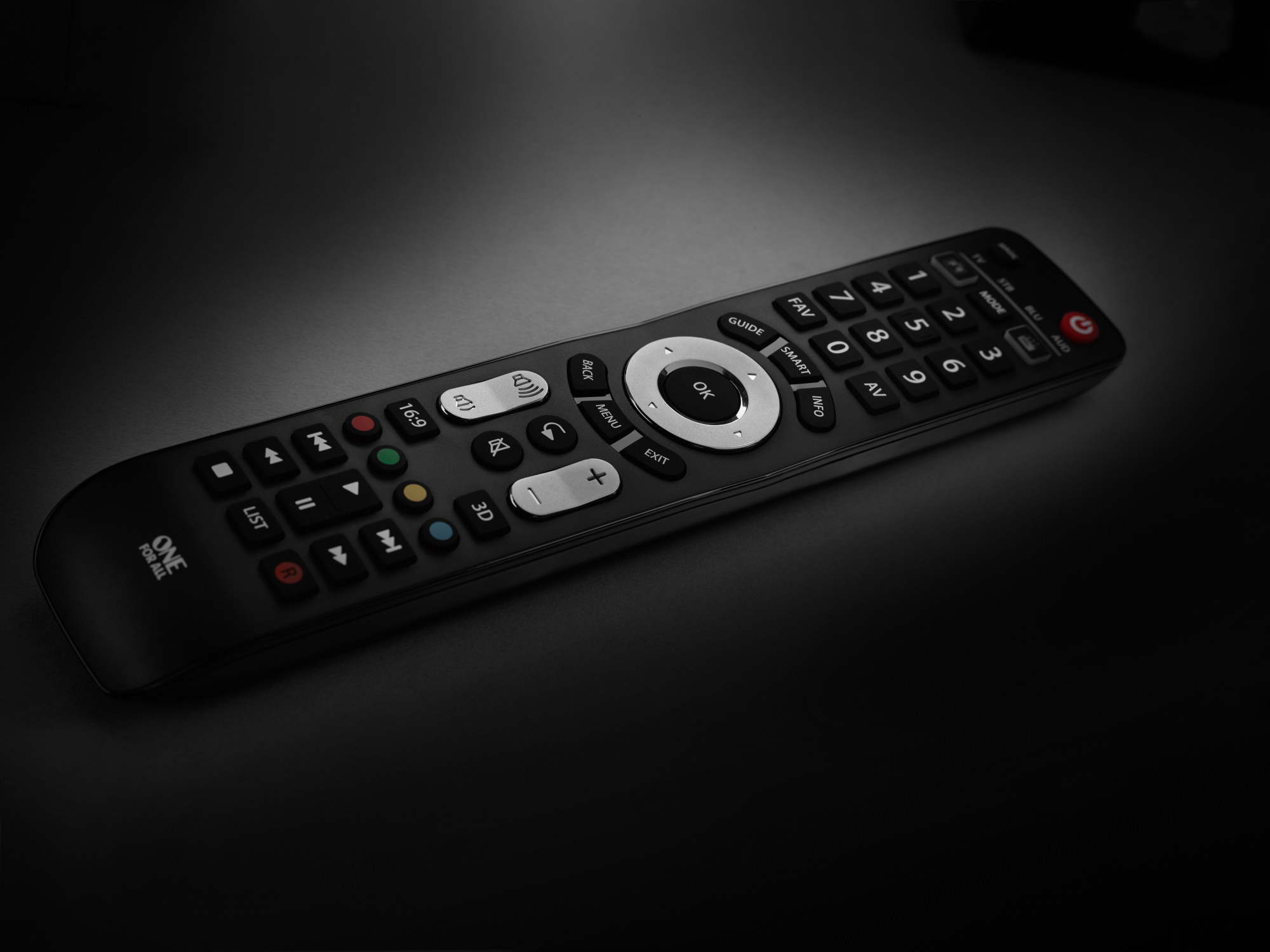 Eine schwarze TV-Fernbedienung auf dunkler Oberfläche. Die Fernbedienung hat viele Knöpfe.