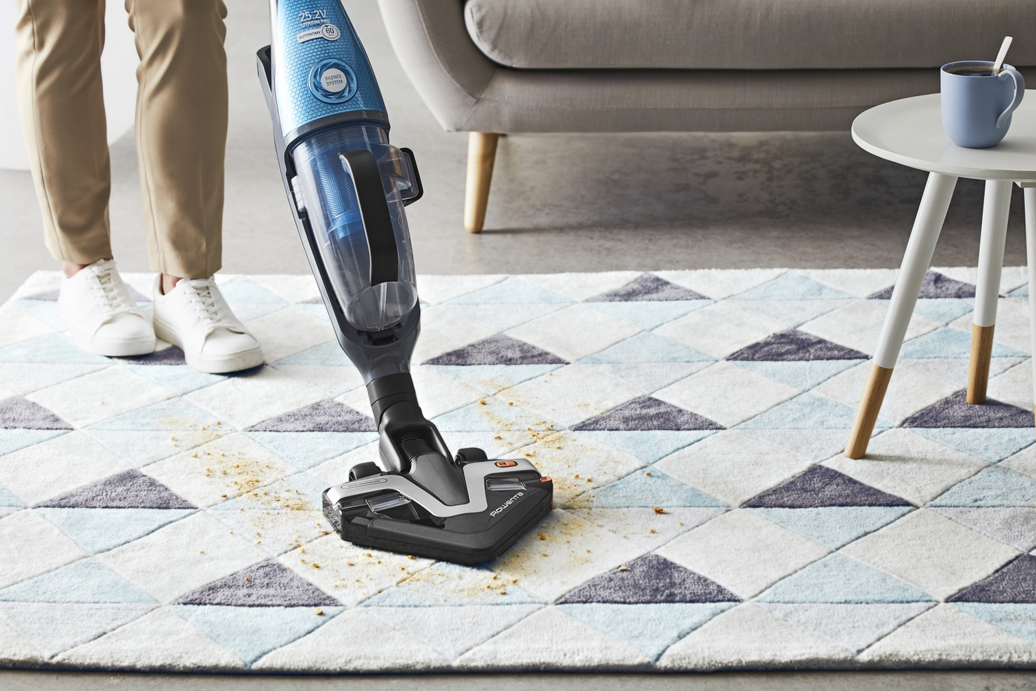 Persona aspirando una alfombra con una aspiradora sin cable. La alfombra tiene estampado.