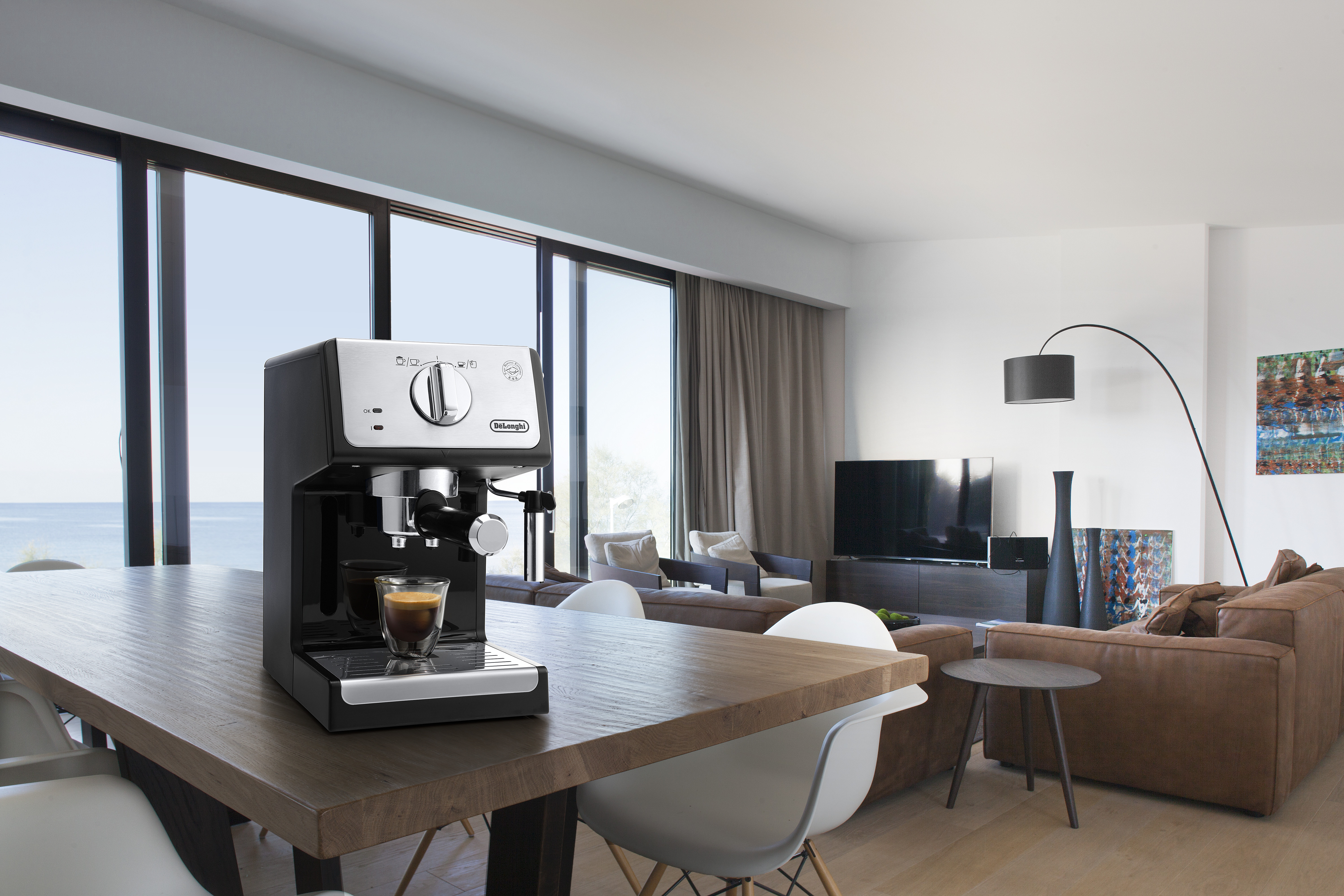 Espressomachine op een houten tafel in een moderne woonkamer met uitzicht op de oceaan.