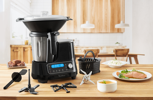Robot de cocina negro con accesorios en mesa de madera.