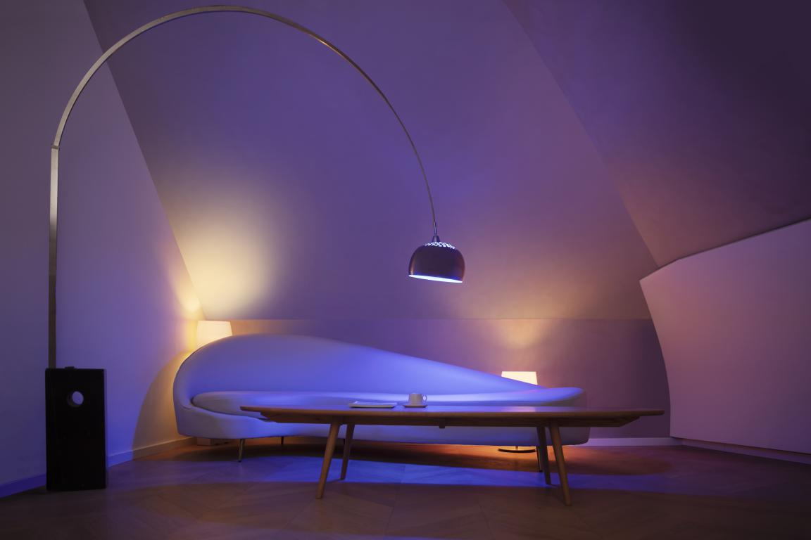 Interior moderno con sofá blanco curvo, mesa de madera, lámpara de arco y lámpara colgante oscura en una habitación con paredes anguladas.