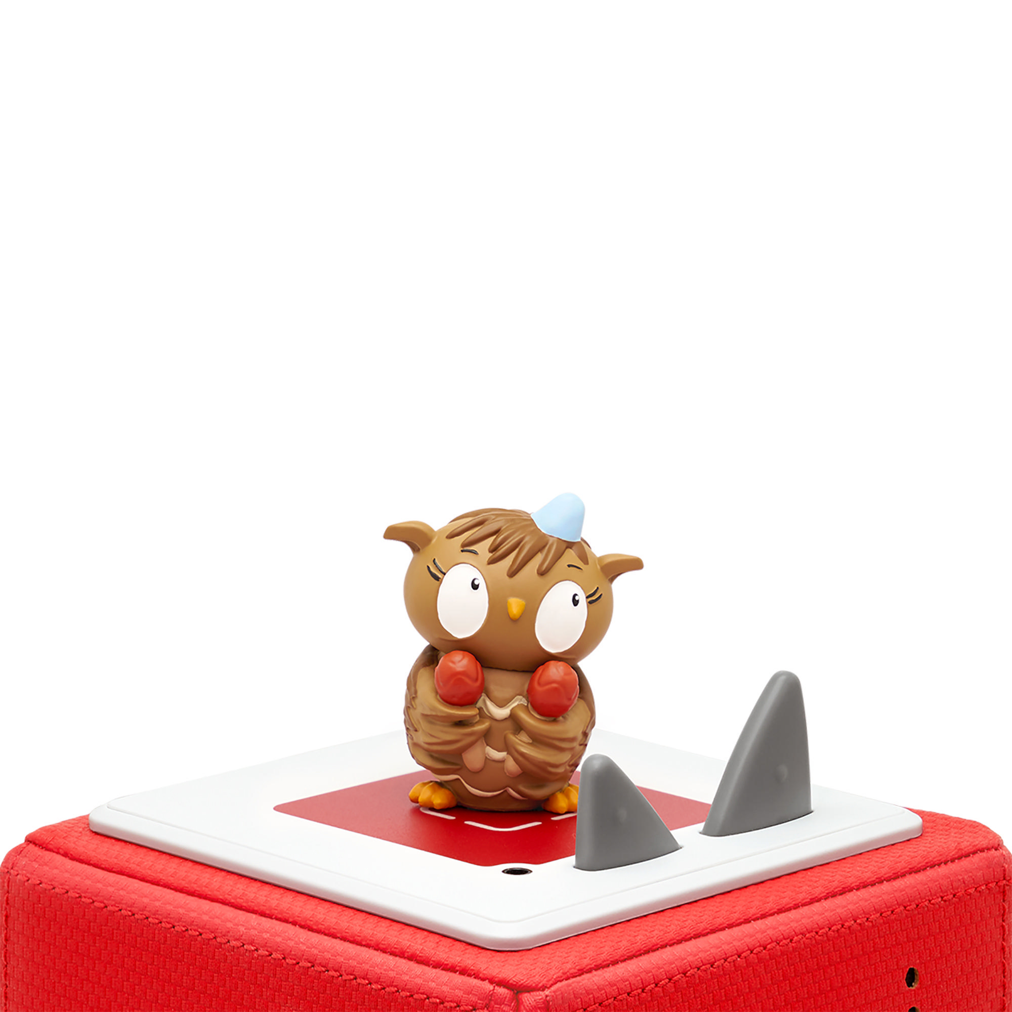 Eine Spielzeug-Eulenfigur auf einer roten Plattform mit Haifischflossen. Weißer Hintergrund.