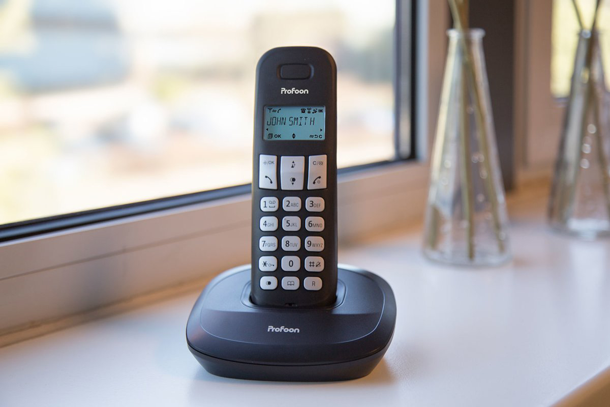 Un téléphone sans fil noir sur son socle avec l'écran affichant 'John Smith'.