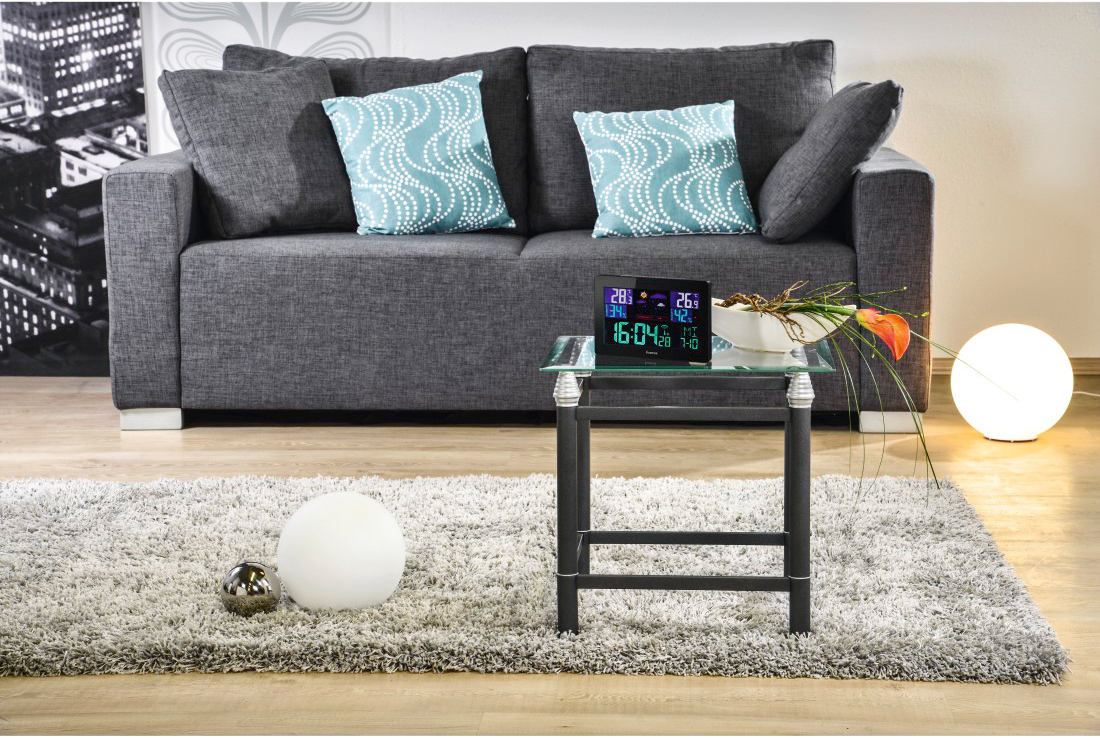 Graues Sofa mit blauen Kissen, Glastisch mit Wetterstation und runde Lichter.