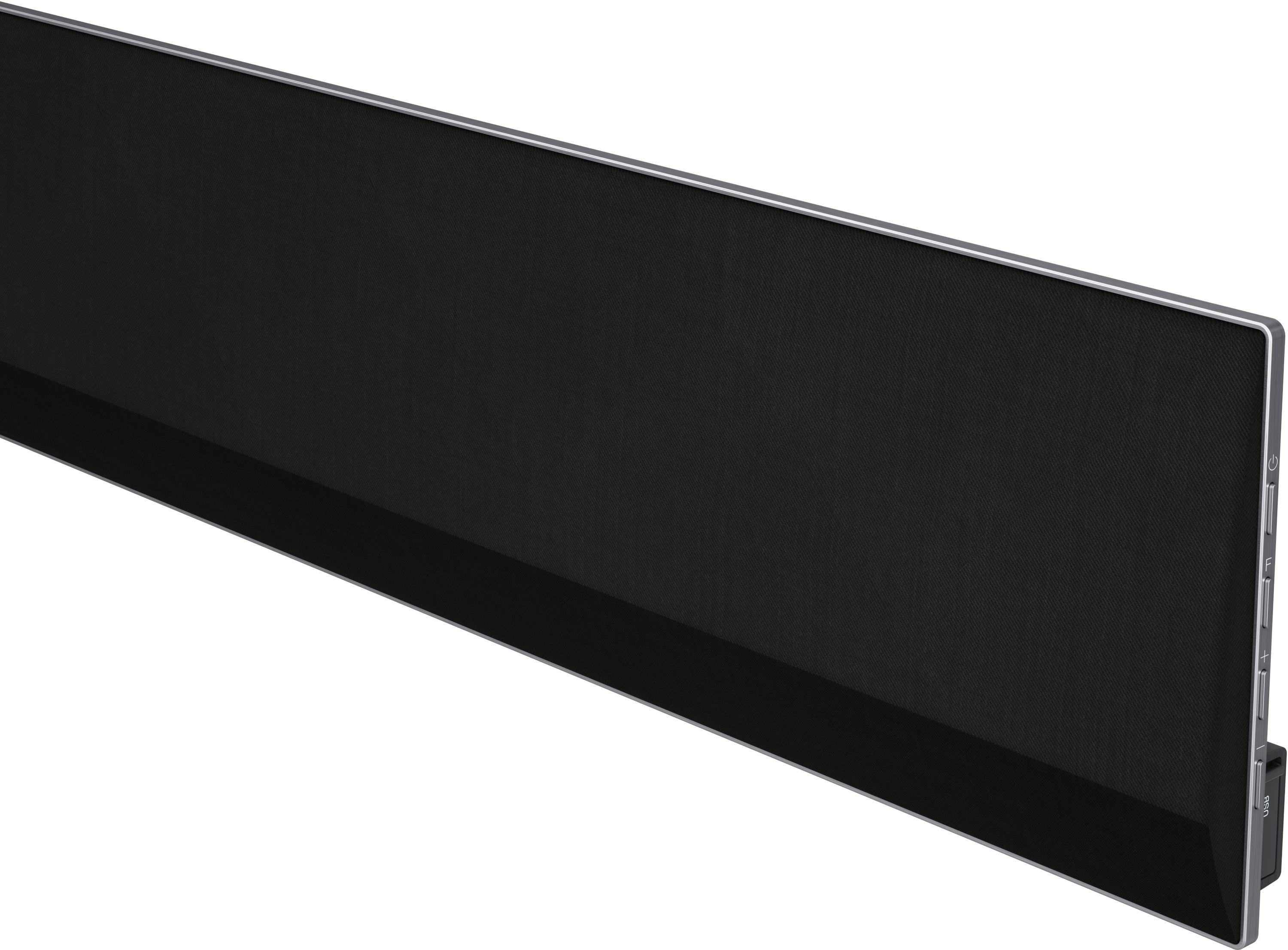 Eine lange, schwarze Soundbar mit silberner Zierleiste. Es ist an einer Wand positioniert, mit schwarzem Stoff.