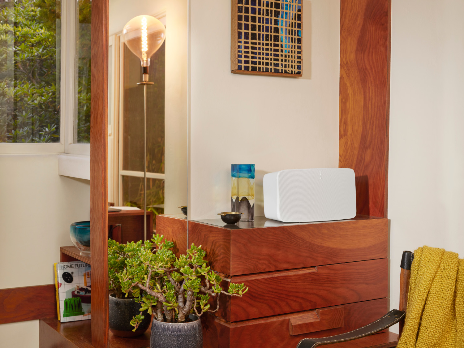 Étagère en bois avec haut-parleur blanc, décor et plantes. Le miroir reflète la pièce.