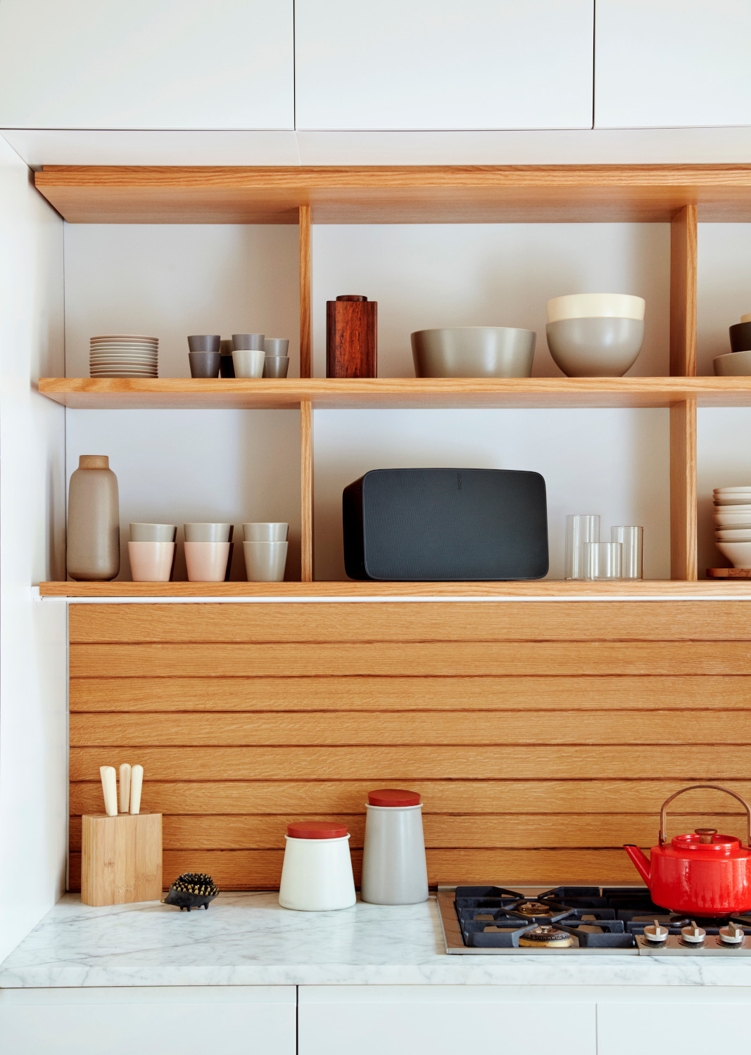 Modern kitchen with wooden shelves holding items; marble countertop, and a red teapot.
