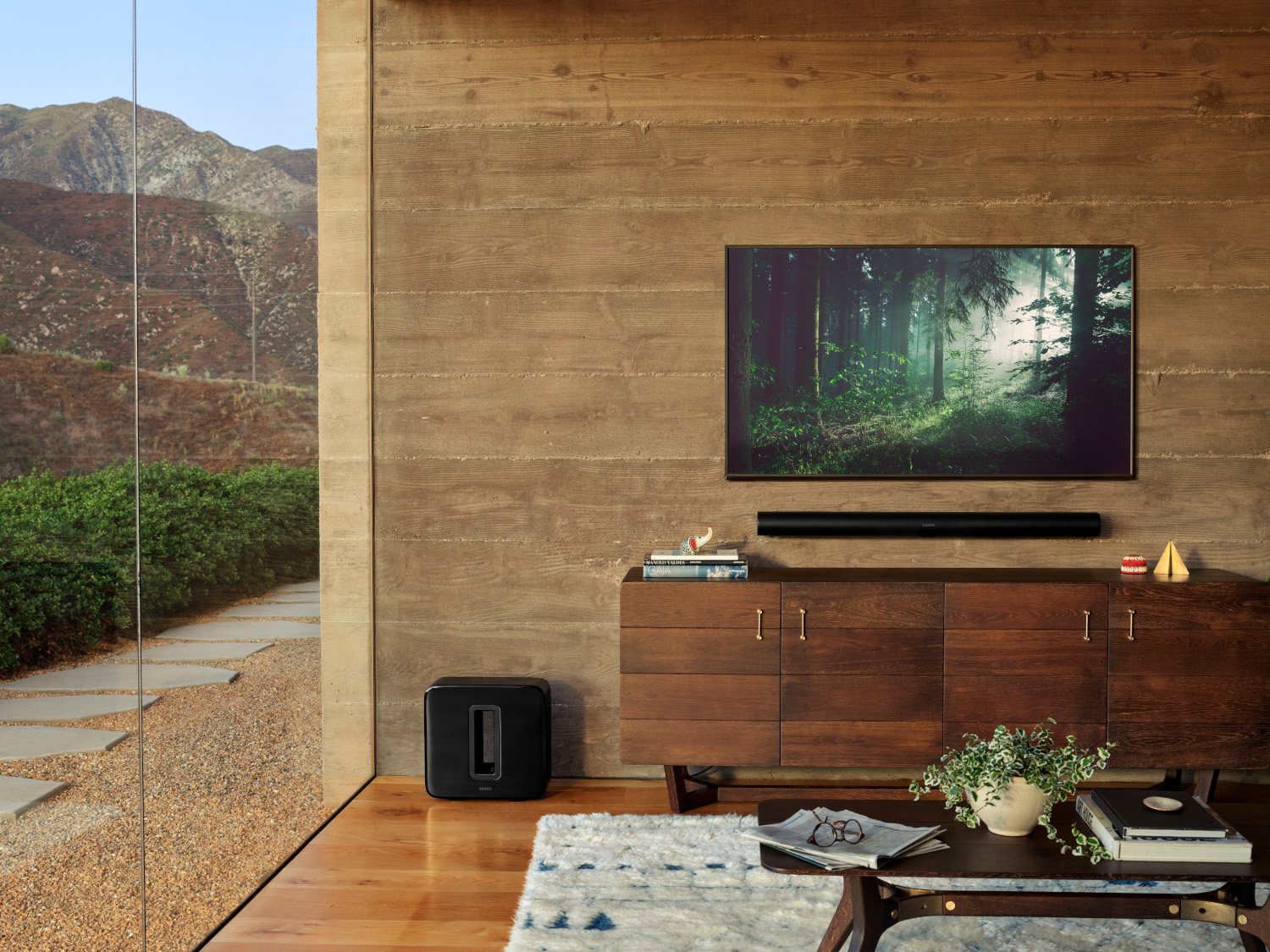 Woonkamer met een tv op een houten kast en een soundbar. Een zwarte subwoofer op de vloer.