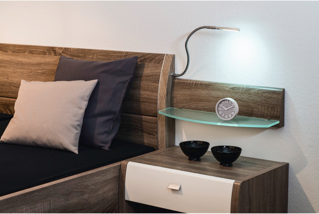 Une chambre avec un lit, des oreillers, une table de chevet et une lampe avec une horloge.