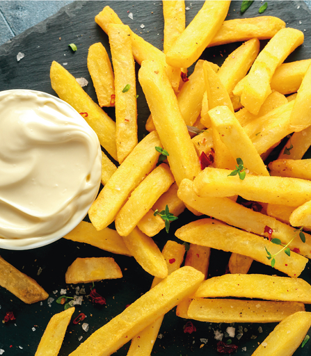Papas fritas y un cuenco de mayonesa sobre una superficie oscura.