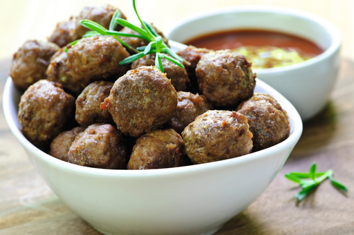 Un bol de albóndigas con ramita de romero y salsa en superficie de madera.