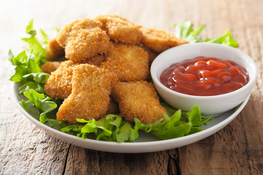 Nuggets de pollo en un plato con lechuga y un cuenco pequeño de ketchup sobre una mesa de madera.